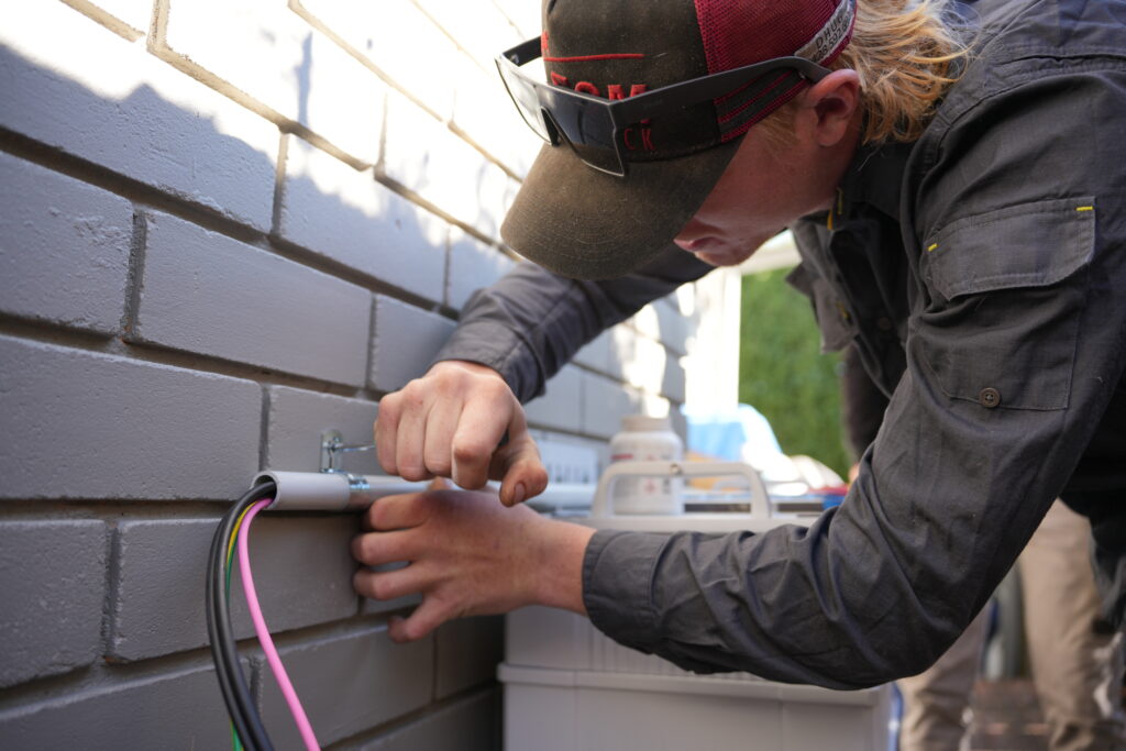 team member from Lenergy installing a Sungrow battery on home exterior in Moss Vale