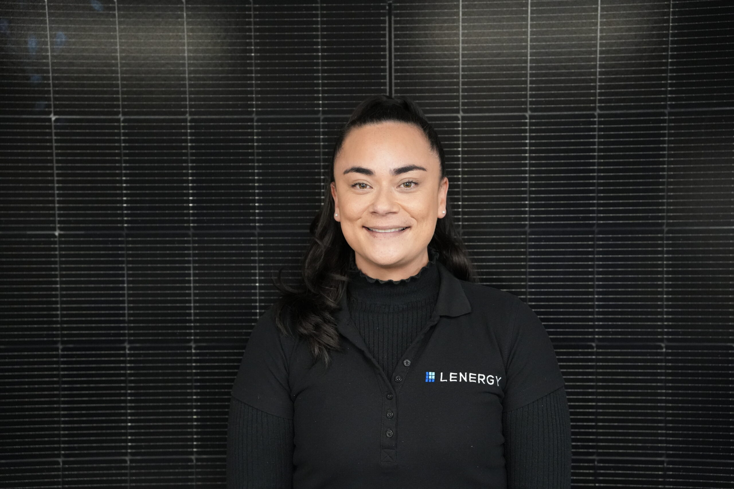 A team member from Lenergy standing in front of a panel, smiling with a black branded polo with a Lenergy logo