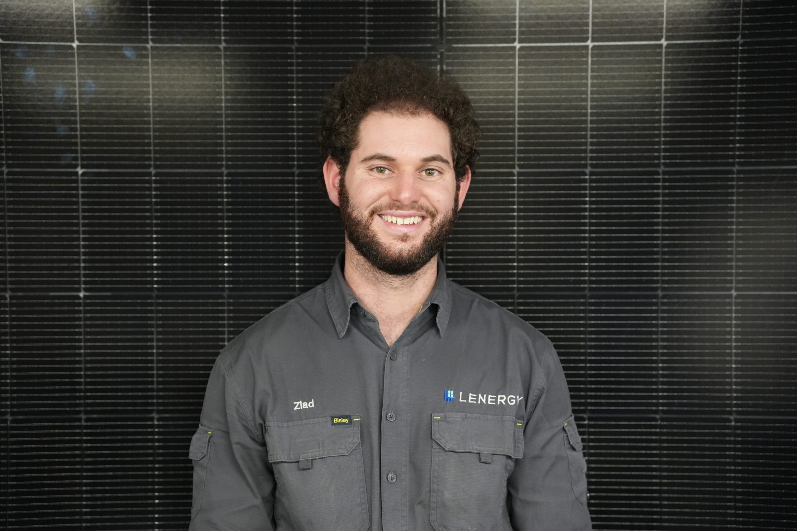Lenergy staff member, Ziad standing in front of solar panels smiling