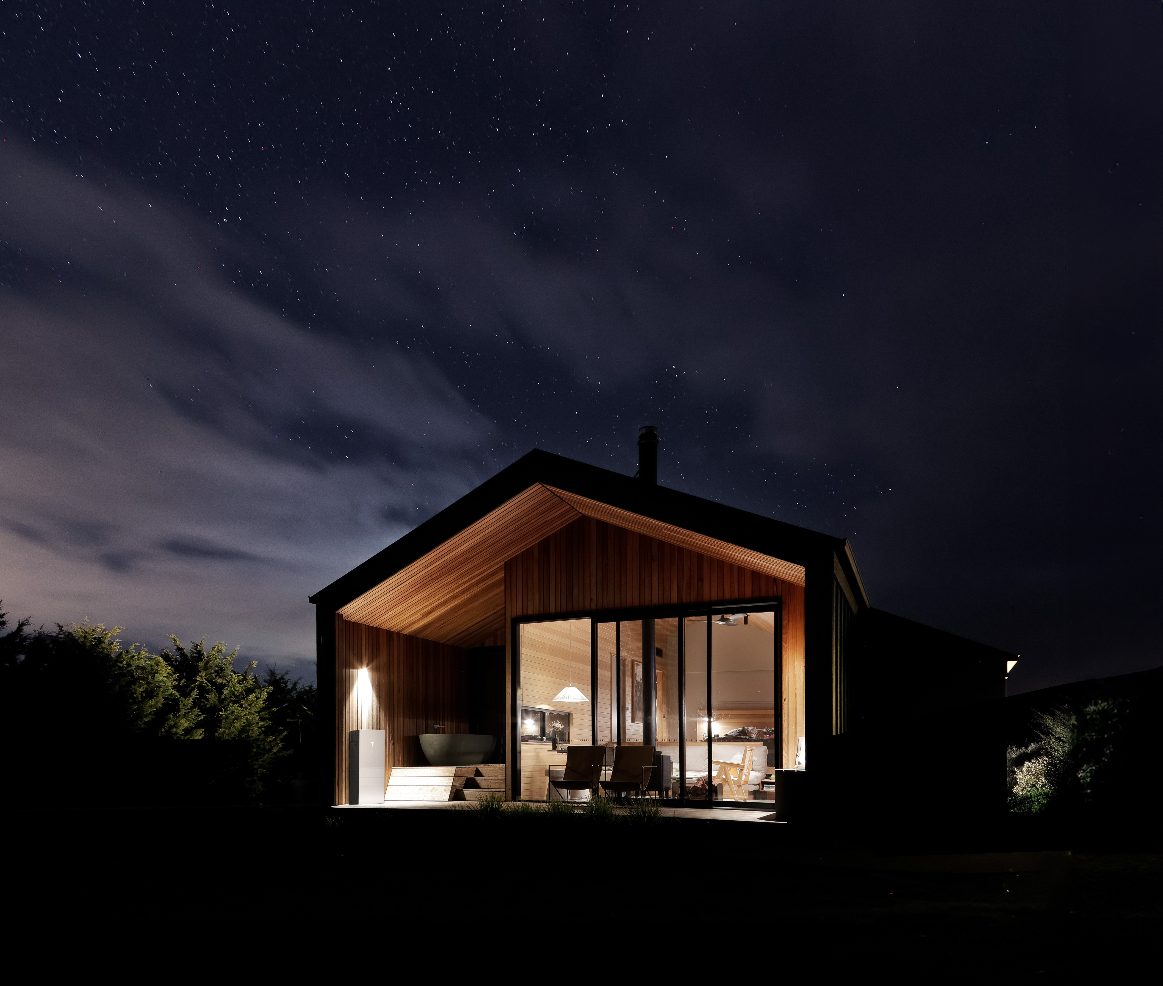 An image of a home lit up at night with a Tesla Powerwall 3 glowing and provided power to the home.