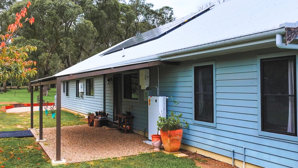 Modern home with rooftop solar panels, inverter and battery system installed beside the entrance on an exterior wall.