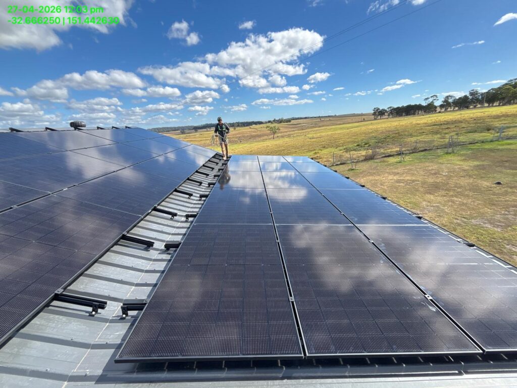 Solar panels on a metal roof with a technician working, rural landscape beyond, with visible timestamp and GPS coordinates overlay in top corner
