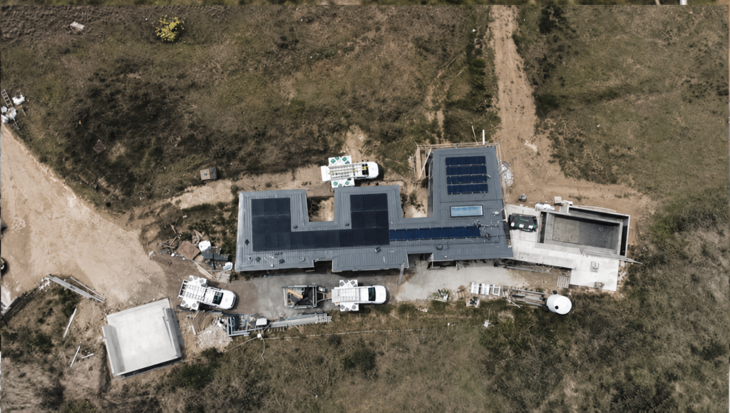 Aerial view of the off-grid Kangaroo Valley property showing three solar arrays across the roof, with rural paddocks and a dirt access track surrounding the house