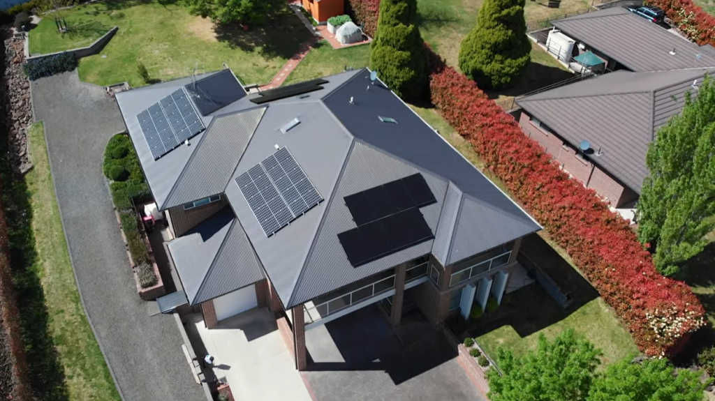 Aerial view of a large Moss Vale home with several rooftop solar panel arrays across a grey roof.