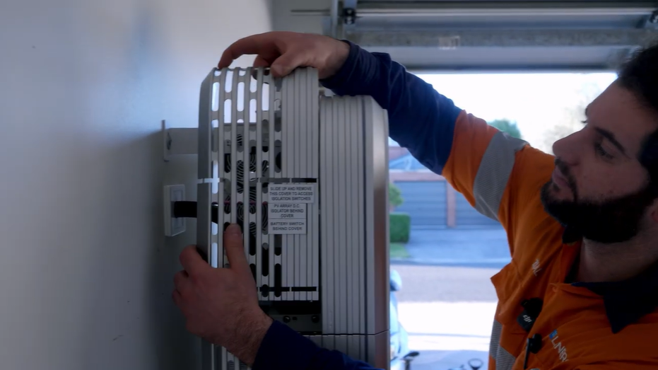 Technician Ziad sliding off the cover to reach the DC isolator and battery switch when resetting the SigenStor Wi-Fi connection.