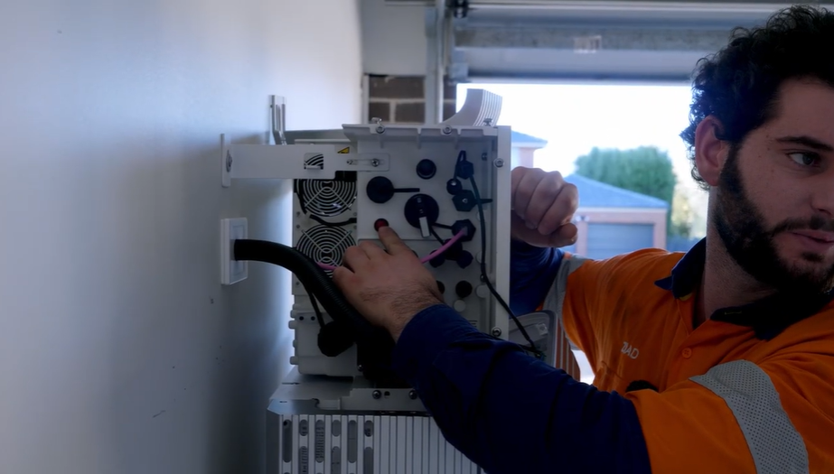 Technician Ziad reaching for the red on/off switch and DC isolator on the SigenStor to power cycle and reset its Wi-Fi connection.