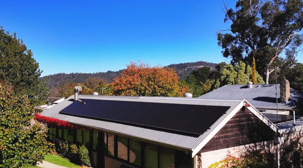 Black solar panels from Helen's solar and battery system installation on a north-facing metal roof in Welby, with the Southern Highlands behind.