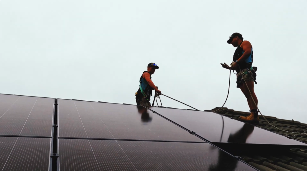 Two harnessed Lenergy installers fitting Suntech solar panels to Colin's tiled roof, the array that powers his air conditioner with solar power.