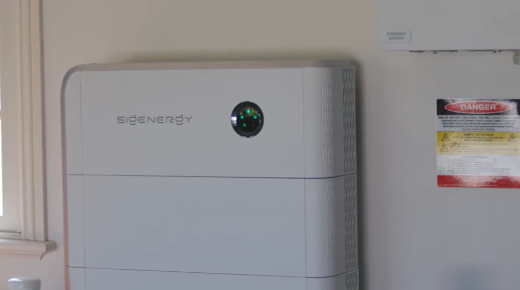 A wall-mounted home battery system with a status indicator light and gateway unit installed in a residential space.